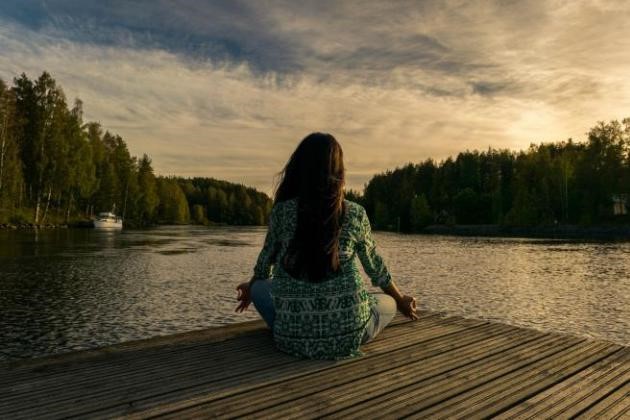 Jeune femme qui médite au bord d'un lac en fin de journée 